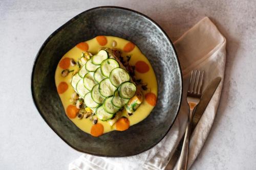 a bowl of soup with cucumbers and carrots on a table at The Ellison, Oklahoma City, a Tribute Portfolio Hotel in Oklahoma City