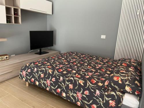 1 dormitorio con 1 cama con manta de flores y TV en Casa di Laura mono e bilo di fronte Ospedale San Raffaele, en Segrate