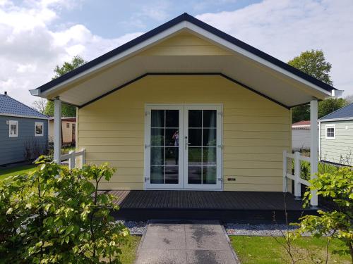 a small yellow house with a porch at De Bijsselse Enk, Noors chalet 18 in Nunspeet