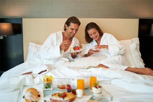 a man and a woman sitting in bed with food at The Westin Kuala Lumpur in Kuala Lumpur