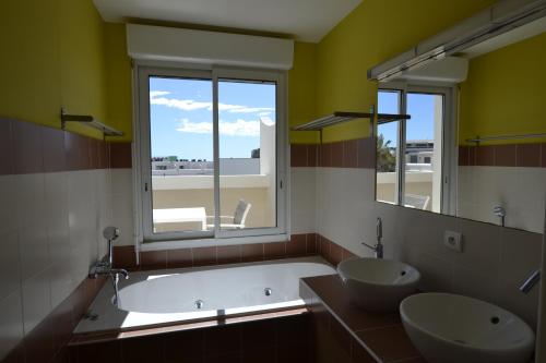 La salle de bains est pourvue d'une baignoire, de 2 lavabos et d'une fenêtre. dans l'établissement Studio Ève Résidence Naturiste Le Jardin D'Eden, au Cap d'Agde