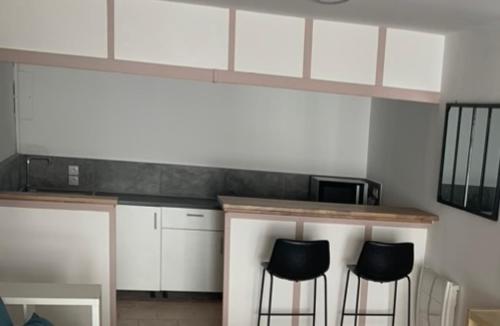 une cuisine avec deux tabourets noirs à un comptoir dans l'établissement GRAND STUDIO AU CALME, à Nîmes