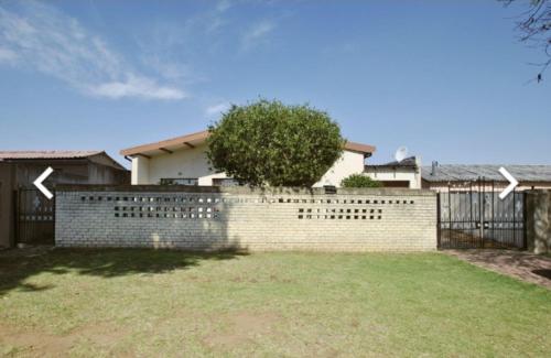 a brick fence in front of a house with a tree at House of creations in Diepkloof