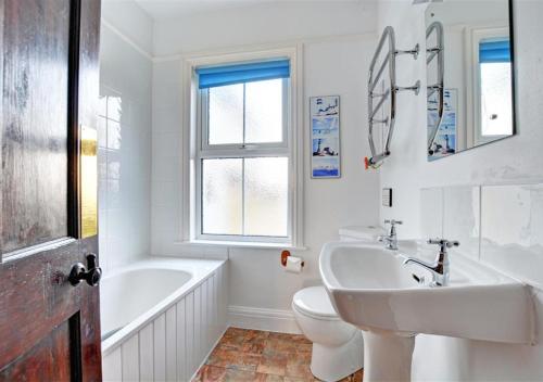a white bathroom with a sink and a tub and a toilet at Trearth in St Merryn
