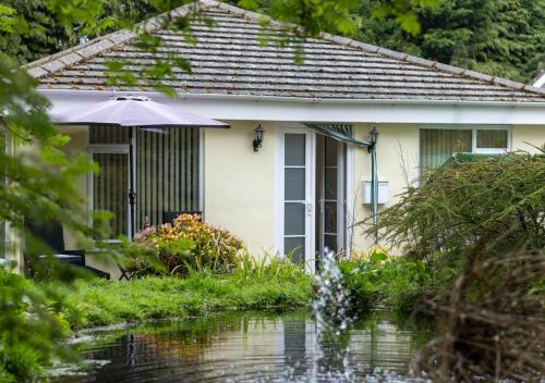 a house with an umbrella and a pond in front of it at Monkey Puzzle Retreat in Belford