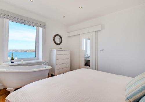 a white bedroom with a bed and a tub and a window at The Lookout - Sennen in Sennen