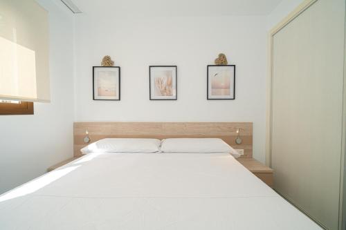 1 dormitorio con 1 cama blanca grande y 3 cuadros en la pared en Nina, en San Juan de los Terreros