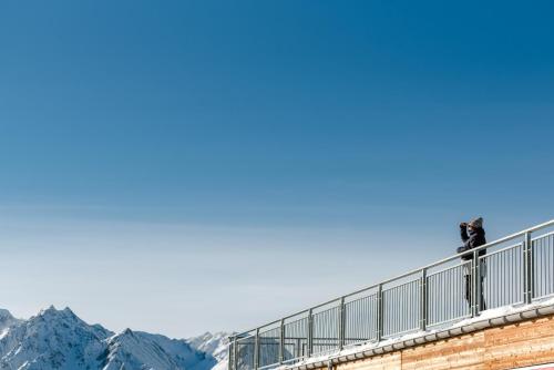 a person standing on a railing with mountains in the background at Aktiv Hotel & Spa Hannigalp in Grächen