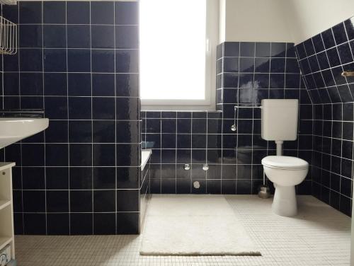 uma casa de banho com azulejos pretos, um WC e um lavatório. em Ferienwohnung Gasthof Port em Naunheim