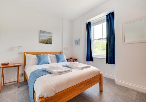 a bedroom with a bed with blue curtains and a window at Capricorn in Saint Levan