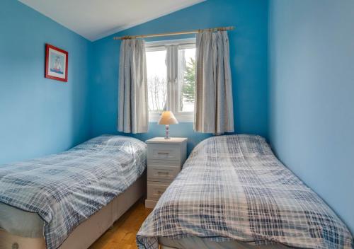 two beds in a blue bedroom with a window at Pine Tree Cabin in Saint Merryn