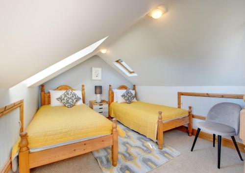a attic bedroom with two beds and a chair at Bay Cottage in Gorran Haven