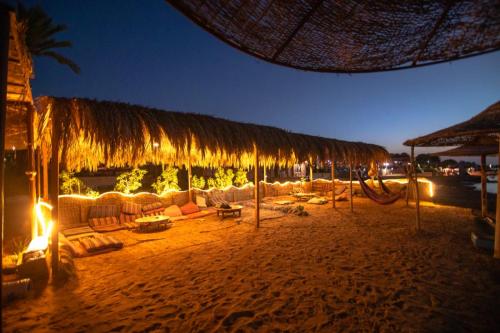 a beach with a straw umbrella and chairs and tables at Elbadawy camp in Nuweiba