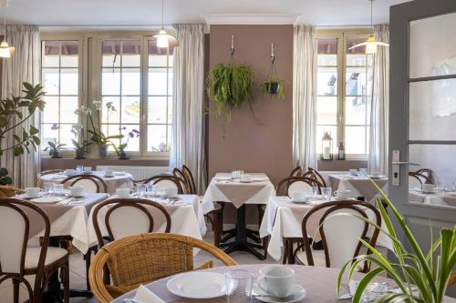 a restaurant with white tables and chairs and windows at Hôtel de Lion sur Mer in Lion-sur-Mer