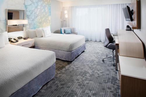 サンドストンにあるCourtyard by Marriott Richmond Airportのベッド2台とデスクが備わるホテルルームです。
