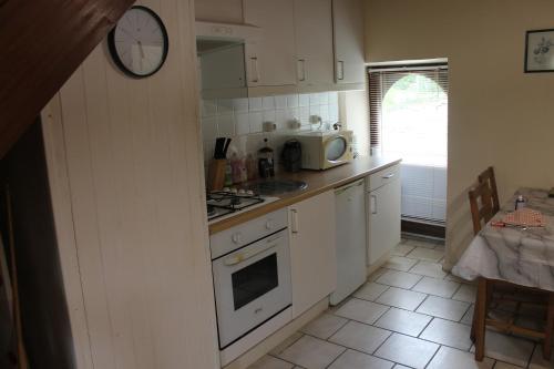 una cocina con armarios blancos y un reloj en la pared en Genevrier Cottage, en Huelgoat