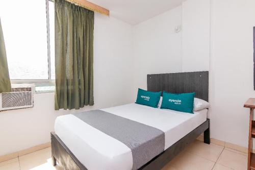 a bedroom with a bed with blue pillows and a window at Ayenda Confort De La Guajira in Ríohacha