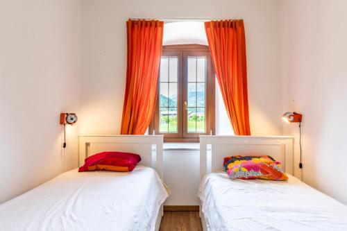 duas camas num quarto com uma cortina laranja em Il Giardino ai Volti 2P, Caldonazzo Ospitar em Caldonazzo