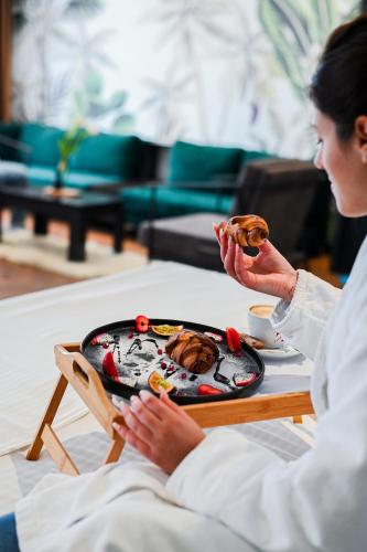 a woman sitting in a bed with a plate of food at Royal G Max in Golem