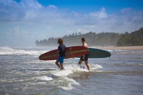 two people walking into the ocean with their surfboards at Barracuda Boutique in Itacaré