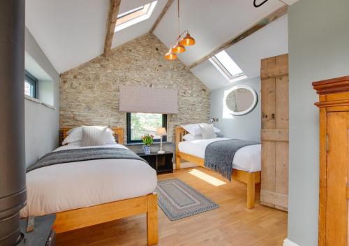 two beds in a room with a stone wall at Higher Treliver Farmhouse Piggery in Saint Wenn