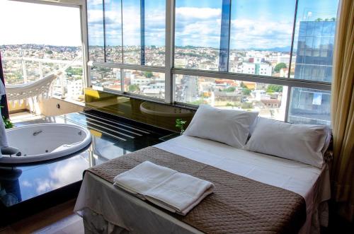um quarto com uma banheira, uma cama e uma janela grande em Manferrari Hotel em Contagem
