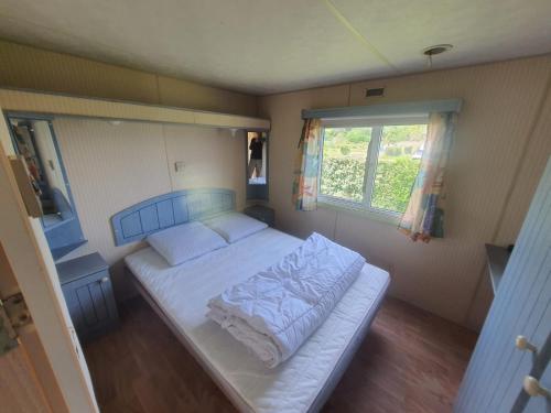 Cama en habitación pequeña con ventana en Camping Village Nature D'O, en Hillion