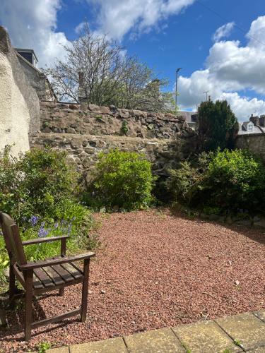 a wooden bench sitting in front of a stone wall at Boston House- Historic house situated in beautiful market town in Duns