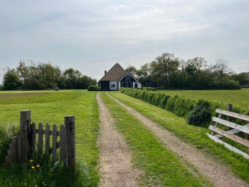 ein Haus auf einem Feld mit einem Zaun und einer unbefestigten Straße in der Unterkunft Zuid Haffel in Den Burg