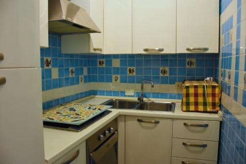 una cucina con armadi bianchi, lavandino e piastrelle blu di appartamento Romi a Porto Cervo
