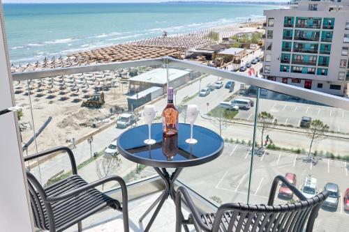 a table with a bottle and two chairs on a balcony with the beach at Scorpios in Infinity Pool & Spa Resort in Mamaia Sat/Năvodari