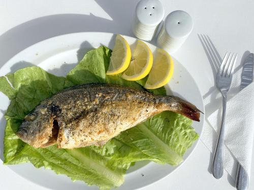 a fish on a plate with lettuce and lemon slices at Apsenti couples only in Agios Ioannis Mykonos