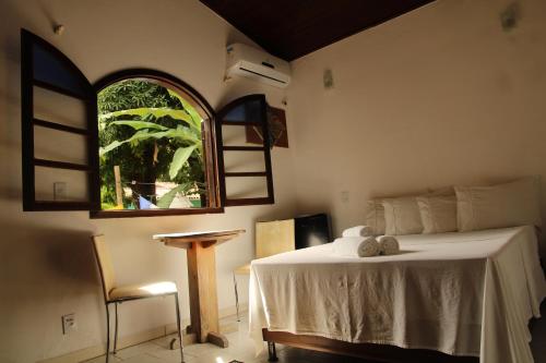 a bedroom with a bed and a window and a table at Hospedaria Bem Te Vi Arraial d'Ajuda in Arraial d'Ajuda