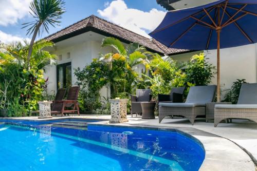 a swimming pool with chairs and an umbrella next to a house at Bakti Villa in Ubud