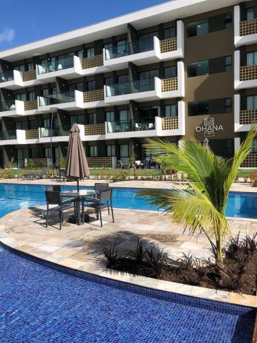 a hotel swimming pool with a table and a umbrella at Mana Beach Experience Muro Alto C219 in Porto De Galinhas