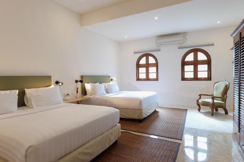 a hotel room with two beds and a chair at Kresna By The Sea By Kresna Hospitality in Seminyak