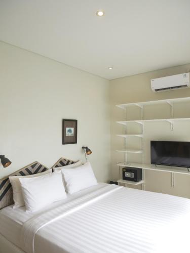 a bedroom with a large white bed and a flat screen tv at Kresna By The Sea By Kresna Hospitality in Seminyak