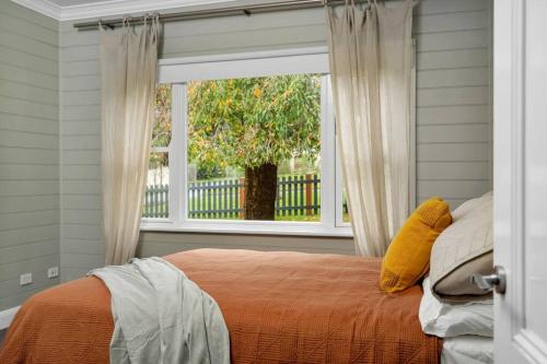 a bedroom with a bed with an orange bedspread and a window at Quarry Hill Cottage, 1 minute walk into Berrima. in Berrima