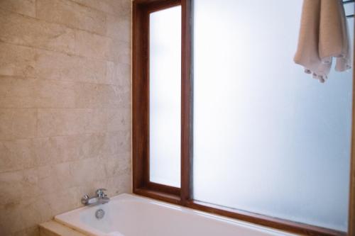 a bathroom with a bath tub and a window at Kresna By The Sea By Kresna Hospitality in Seminyak