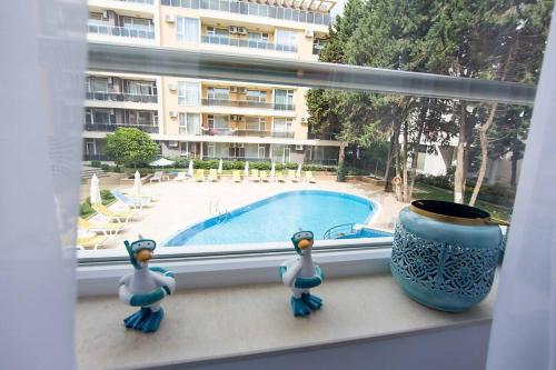 a window with two figurines on a window sill with a swimming pool at Pearl in Ravda