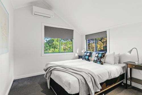 a white bedroom with a large bed and two windows at Fuller Holidays - Leah's Retreat - Relax in nature in Bangalow