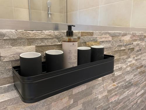 a black bathroom shelf with a bottle and four cups at Airport Apartments for 4 - Kitchen - Parking with eCharging in Hamburg