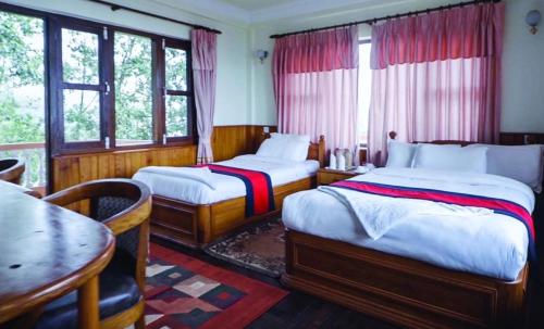 1 dormitorio con 2 camas, mesa y ventanas en Nagarkot Sunshine Hotel, en Nagarkot
