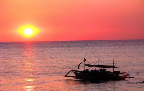 a boat in the ocean with a sunset at Bakasyunan Resort and Conference Center - Zambales in Iba