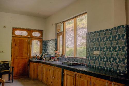 a kitchen with a sink and some windows at Apple Blush Retreat - Tirthan Valley in Gushaini