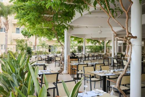 an outdoor restaurant with tables and chairs and trees at Sunrise Oasis Hotel & Waterpark in Protaras