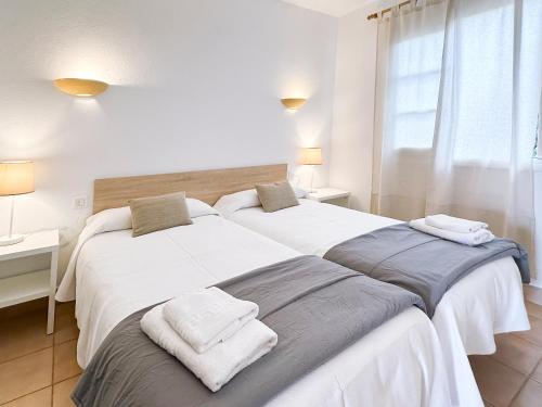 Dos camas en un dormitorio blanco con toallas encima. en Grupoandria Aparthotel Club Andria, en Cala Santandria