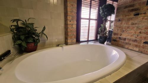 een groot wit bad in een badkamer met een plant bij Klein Bosveld Guest House in Witbank