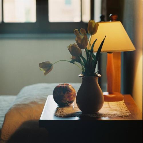 a table with a vase with flowers and a lamp at Residenza Antica Canonica in Città di Castello