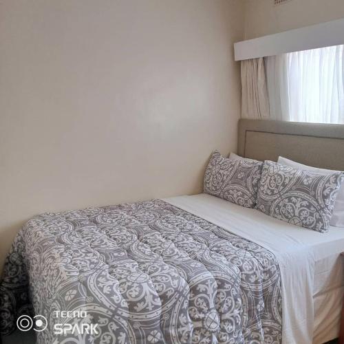 1 dormitorio con 1 cama con edredón gris y blanco en Neat and cosy cottage with pool - 2103 en Harare